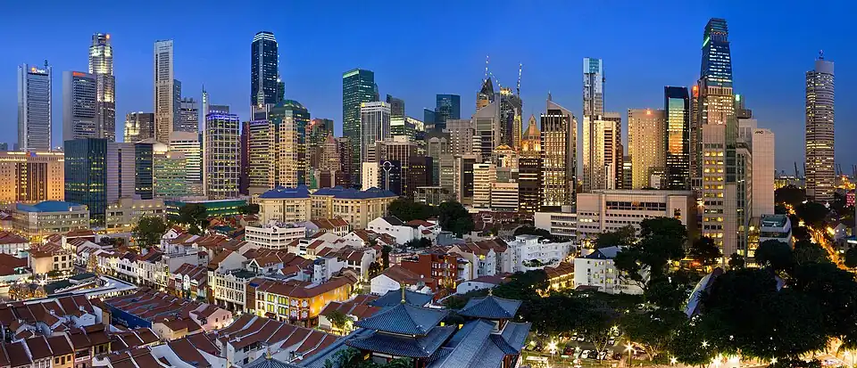 Skyline of a city, showing several tall skyscrapers. The tallest buildings are at the left and right of the image, with several low-rises in the immediate foreground. Most of the towers are lit up, as night is approaching