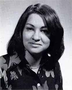 A formal pose of a young woman in her early twenties, dark straight hair parted near the center, wearing a dark floral print top.