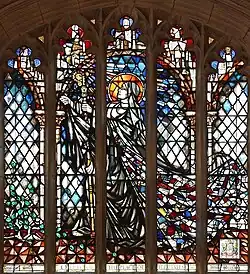 Modern stained glass window of Ethelburga. She is wearing a nun's habit and striding through a cloister, her gaze uplifted towards a source of radiant light.