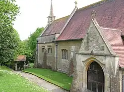 Part of a church built in stone with red tiles and a short spire