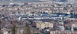 Elevated view of the stadium from a distance, surrounded by smaller buildings