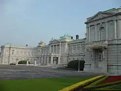 A large palace built of white stone in neo-baroque style. The facade is adorned with colons.