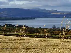 A view of stubble field, a body of water and dark hills beyond