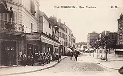 Black and white photograph depicting a square lined with houses and cafés.