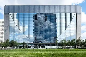 A glass and stone building wider than it is tall, with an inlaid parabolic U shape in the glass across the entire facade.