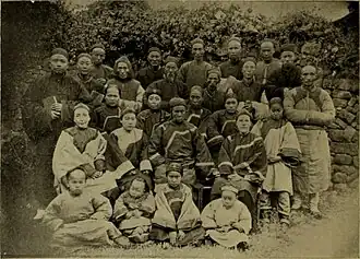 A sepia-toned photograph showing about 20 adults and children dressed in traditional Chinese clothing