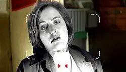 A camera view of a woman lying against a wall, blood dripping out her mouth.