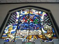 The Battle of Hastings (1066) as depicted on a stained glass window over the main entrance. The French phrase (l'action continue&nbsp;... avec fureur) translates to "the battle rages on".