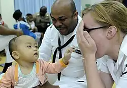 US Navy 100406-N-7478G-346 Operations Specialist 2nd Class Reginald Harlmon and Electronics Technician 3rd Class Maura Schulze play peek-a-boo with a child in the Children's Ward at Hospital Likas