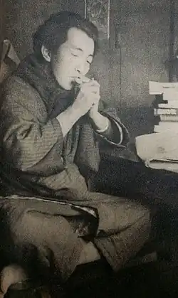 A full body picture of a seated Keinosuke Uekusa smoking.