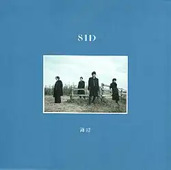 A small photo of the band stood around a wood fence in a field, with a large blue field around it.