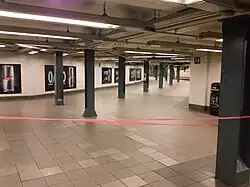 View of a corridor sloping upward from the IRT mezzanine to the BMT mezzanine. The corridor is wide and contains tiled floors, a low ceiling, and green columns.