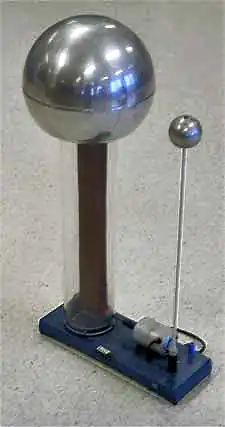 Large metal sphere supported on a clear plastic column, inside of which a rubber belt can be seen clearly: A smaller sphere is supported on a metal rod. Both are mounted to a base plate, on which is a small driving electric motor.