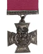 A bronze cross pattée bearing the crown of Saint Edward surmounted by a lion with the inscription FOR VALOUR. A crimson ribbon is attached