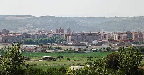 View of some large apartments in Talavera de la Reina with a farmer's field in the foreground, and large hills in the background
