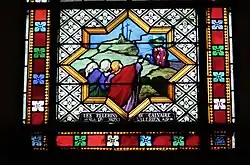 Color photograph of a stained glass window depicting a group of people in front of a mountain.