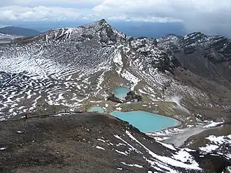 Small blue-green lakes surrounded by patchy snow near a mountaintop