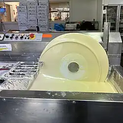 Liquid white chocolate in a machine spins on a wheel, being pulled from a pool of chocolate.