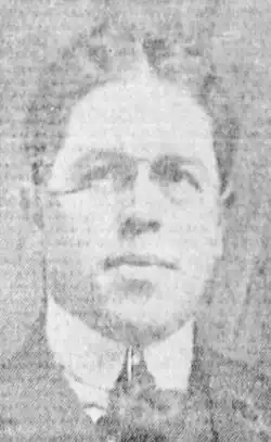 Black and white photo of a middle-aged man wearing eyeglasses, and a white high-collar dress shirt