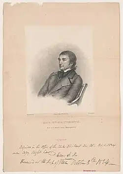 Black and white image from the waist-up of Matthews seated, with a handwritten caption below