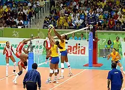 Brazilian and Cuban athletes during a volleyball match wearing the official uniforms of their respective nations. The audience remained watching at the competition venue for the volleyball tournament.