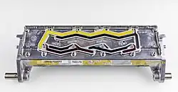 bright yellow and dark colored wax fills raised wavy slots in a die cast aluminum plate. the wax cracked in places where it shrank during cooling and hardening