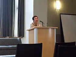 Xu Xi standing behind a podium, speaking into a microphone