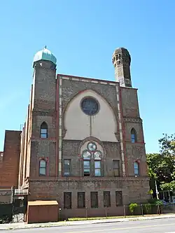 Photograph of the side fascade of building. The decorative brickwork includes complex curved arches and multi-colored details Atop the building are two minarets.