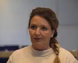 A Caucasian woman with dark-blond braided hair in a white room