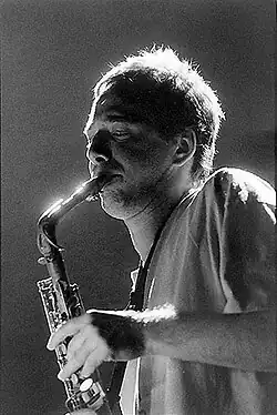 Black and white photo of a man with short hair and a T-shirt playing saxophone