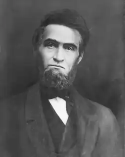 A middle-aged man with a very bushy beard is looking straight at the camera. His head is slanted slightly to viewer's right.