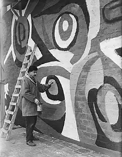 Karel Appel, 1955: Karel Appel is painting on the wall of an exposition-building in Rotterdam - photo, 19 April 1955 by Joop van Bilsen / Anefo - National Dutch Archive