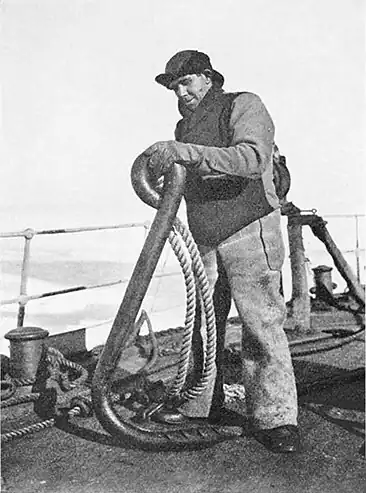 Photograph of a man on the deck of a ship with a chest-height metal hook