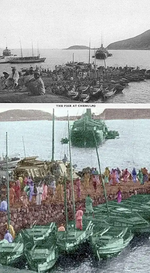 In this picture, there is an earthen pier with several people standing on it and, on the near side of it, several rowboat-sized sailboats are anchored next to it. On the far side of the pear, there appears to be stored defensive artillery. There are some ships in the background. Next to the ships are some of the small boats. It looks like the water around the pier is too shallow for the ships to get next to the pier, so smaller boats are being used to go from the pier to the ships. Beyond the ships, on the left of the picture, the sky meets the sea and on the right side of the picture there are hills between the sky and the water of the bay.