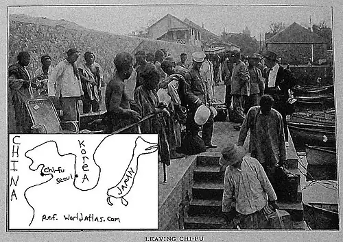 In this photo, several black men are standing around on the sidewalk of a concrete boat dock in China. The dock is in the center and left of the photo; the water is on the right side of the photo. A stairwell next to the water is inset in the dock. On the far side of the stairwell is the top of the stairs. Two black men, facing the viewer, are carrying suitcases down the stairs. The water is calm. Rowboats are tied along the concrete dock, from near to about six rowboats away. Then, the seawall makes a right turn. Beyond the water and the dock are wooden buildings at the top of the photo. They are one and two stories high. A map is sketched lower left which shows where Chi-fu is in relation to Seoul.