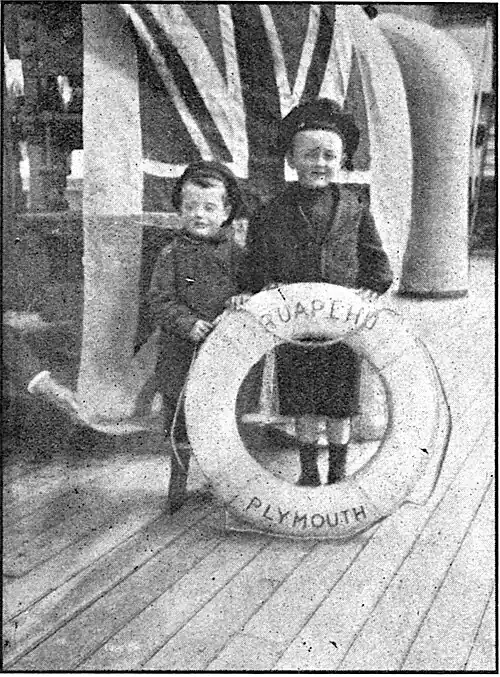 Two small boys on the deck of a ship (the Ruapehu) standing behind a life buoy