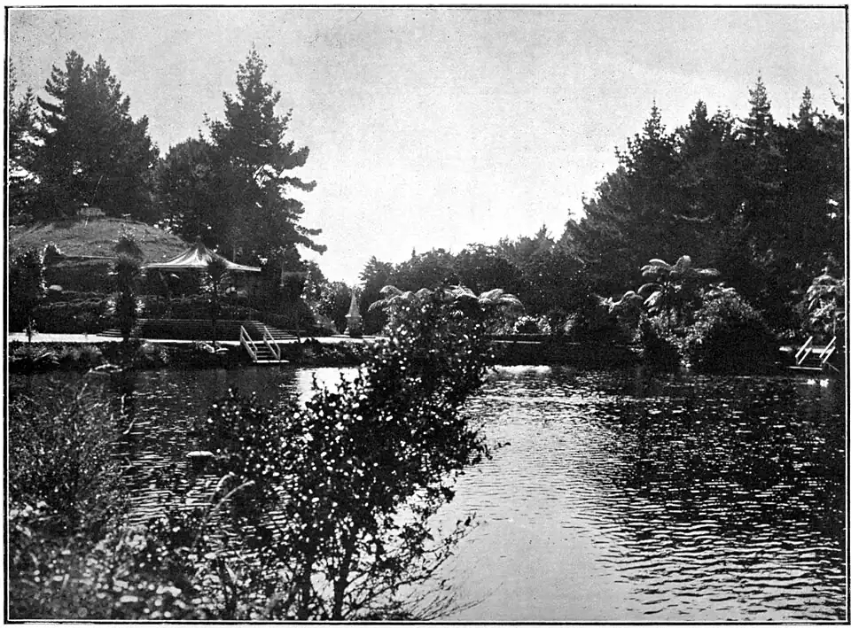 Lake with walkway, sheltered area covered by an awning, trees and tree ferns at New Plymouth Recreation Grounds (Pukekura Park)