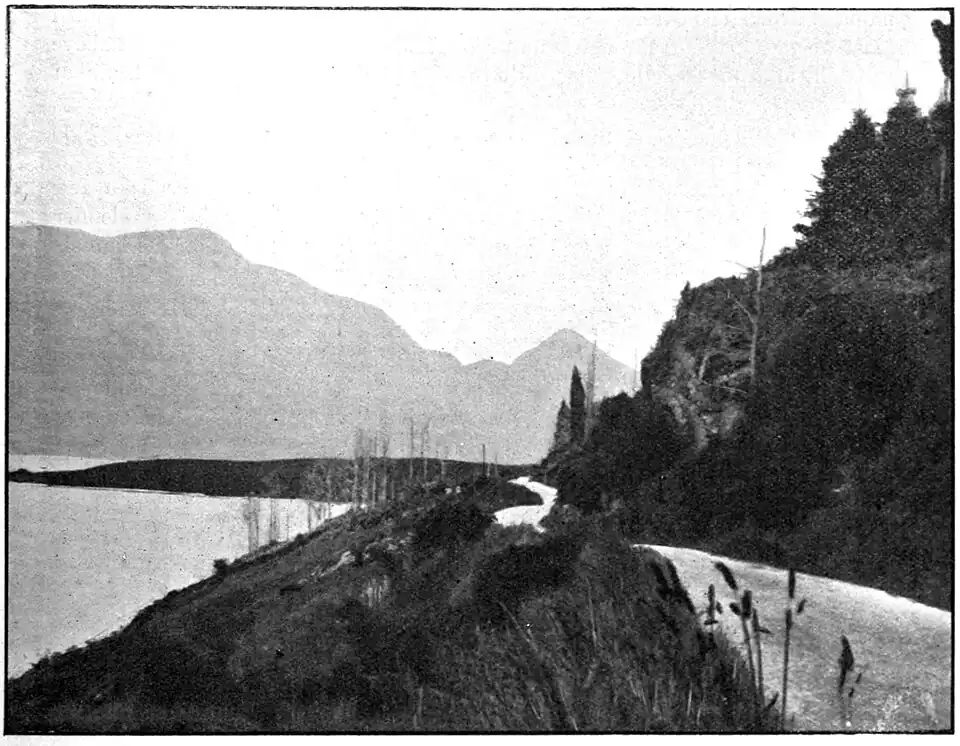 A road beside a lake, mountains in the distance.