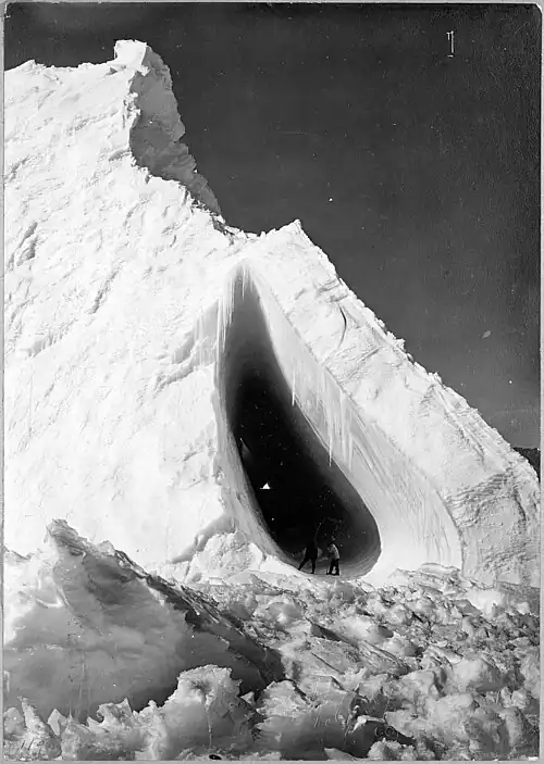 Photo of two men standing in a teardrop-shaped cave in an iceberg