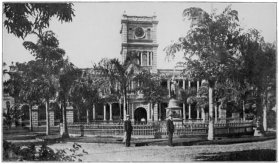 A large building with classical pillars and a tower, surrounded by palm trees