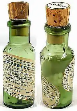 Photograph of two small, corked, green, glass bottles containing small pills. The labels indicate that they contain an old homeopathic remedy called Hepar Sulph.