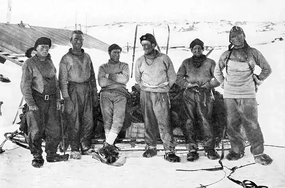 Photograph of six men with dirty faces posing in front of a sledge