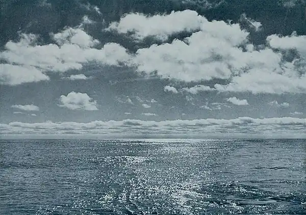 Photo of a calm sunlit open sea with cumulus clouds above