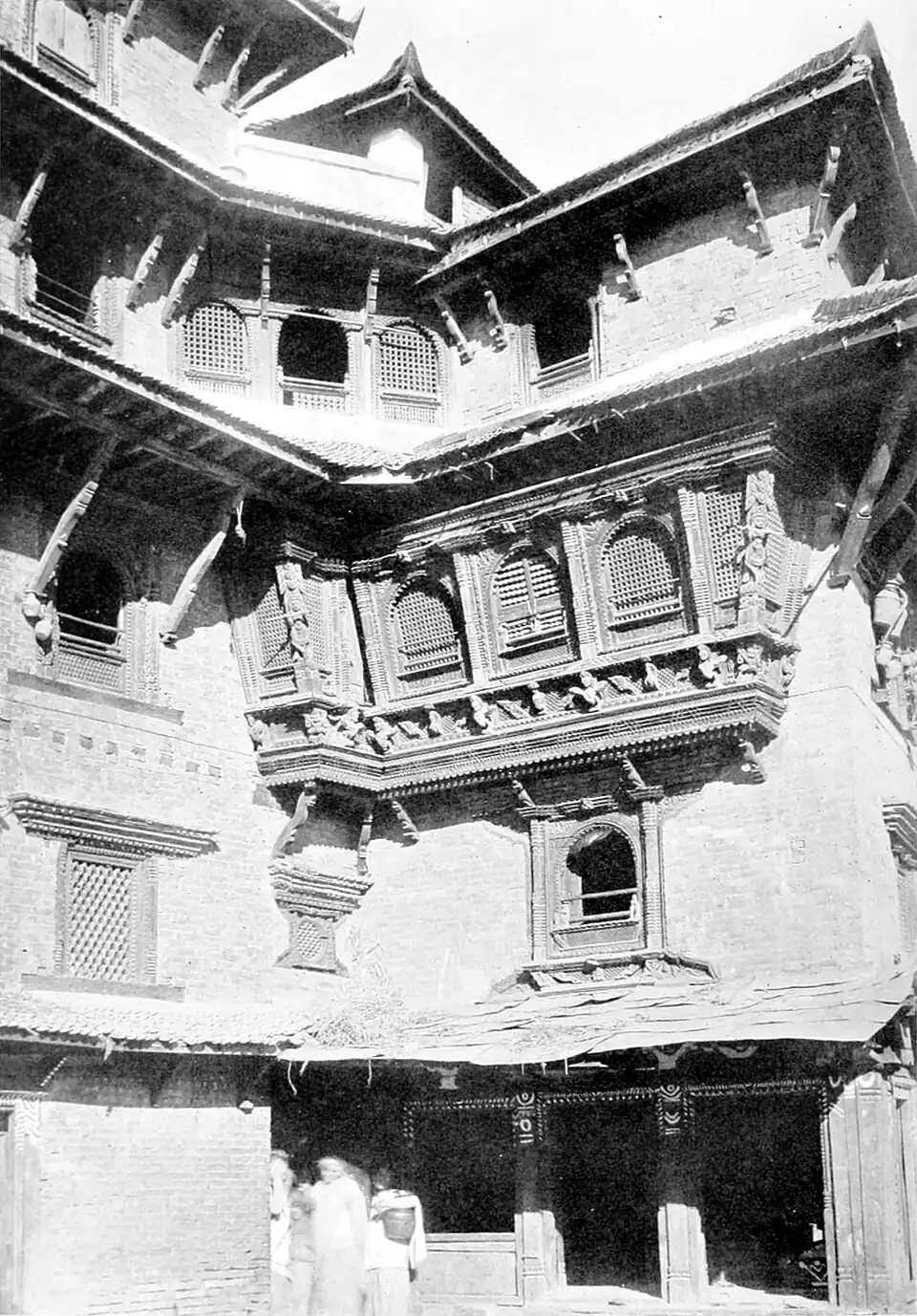 Black and white photograph of the corner of a building. The second or third storey, half way up the wall, features a set of three windows projected out from the wall and covered by grilles. Other windows are not projected, some open and some with grilles.