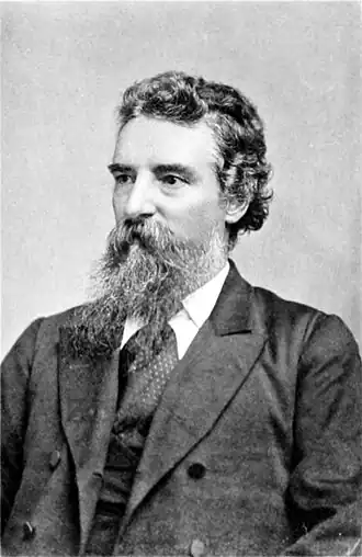 black and white photograph of a man a short dark bears, wearing a suit.