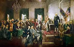 Painting by Howard Chandler Christy of the signing of the Constitution of the United States. George Washington stands on a dais at right with men sitting and standing in the middle third of the painting. The other central figures of the painting are Alexander Hamilton, Benjamin Franklin and James Madison.