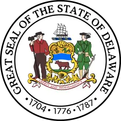 A seal with two men standing on either side of a crest that has a ship on top and features an ox in the center and a banner reading “Liberty and Independence below it”. Around them is a ring reading “Great Seal of the State of Delaware · 1704 · 1776 · 1787”.