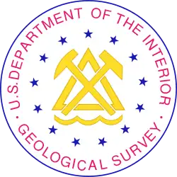 The Seal of the United States Geological Survey. The central element is a crossed pick and hammer, a traditional symbol of mining, over a stylized symbol of a mountain and water.