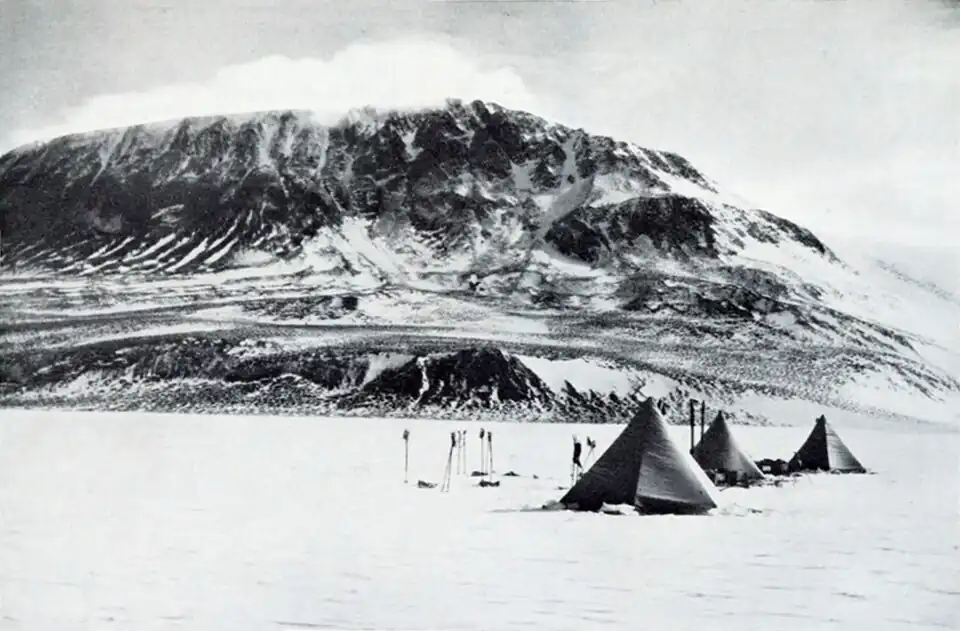 Photograph of three tents on level snow with a large, cloud-topped mountain in the background