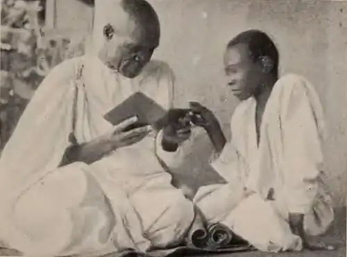 An old man and a boy seated, reading together